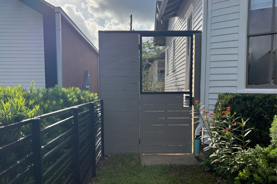 Steel-framed pedestrian side gate with horizontal timber infill and expanded-metal mesh, beside a horizontal-bar steel fence
