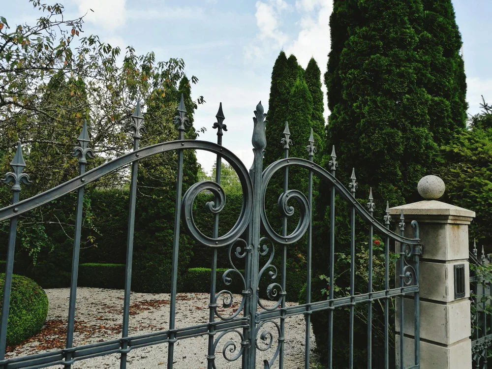 Ornamental steel gate with scrollwork and finials between stone entry columns