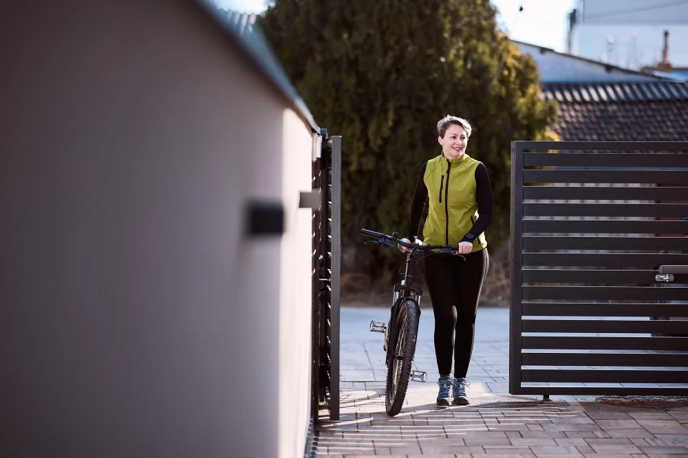 A homeowner walking a bicycle through an open pedestrian gate beside a steel driveway gate