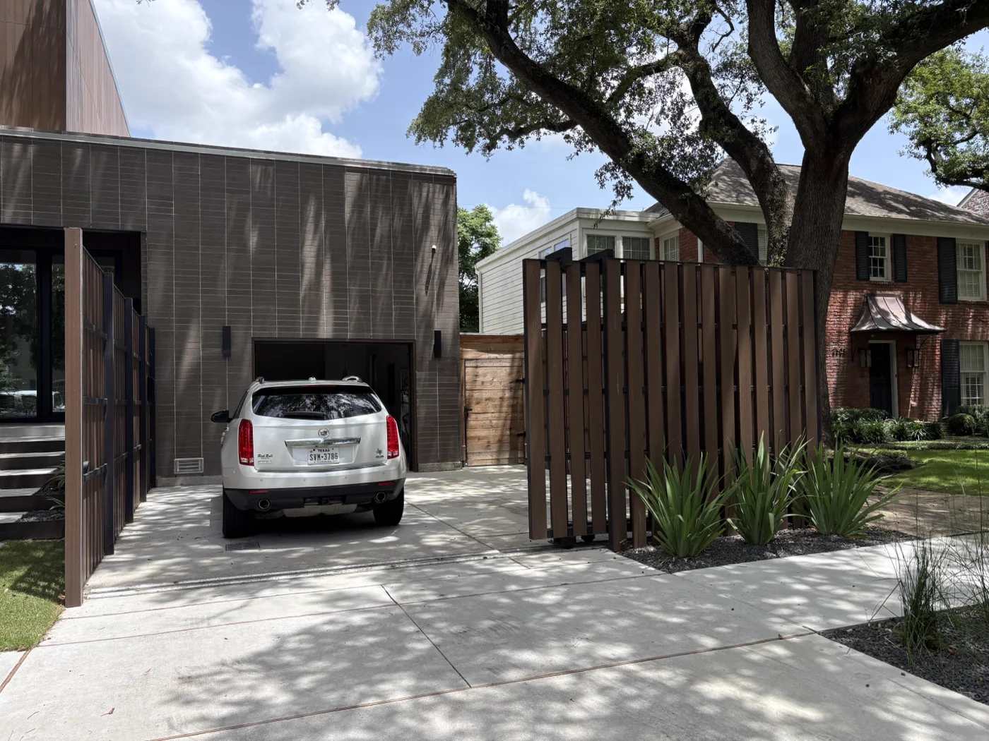 Open sliding steel gate with vertical slats at a modern brick-clad Houston home