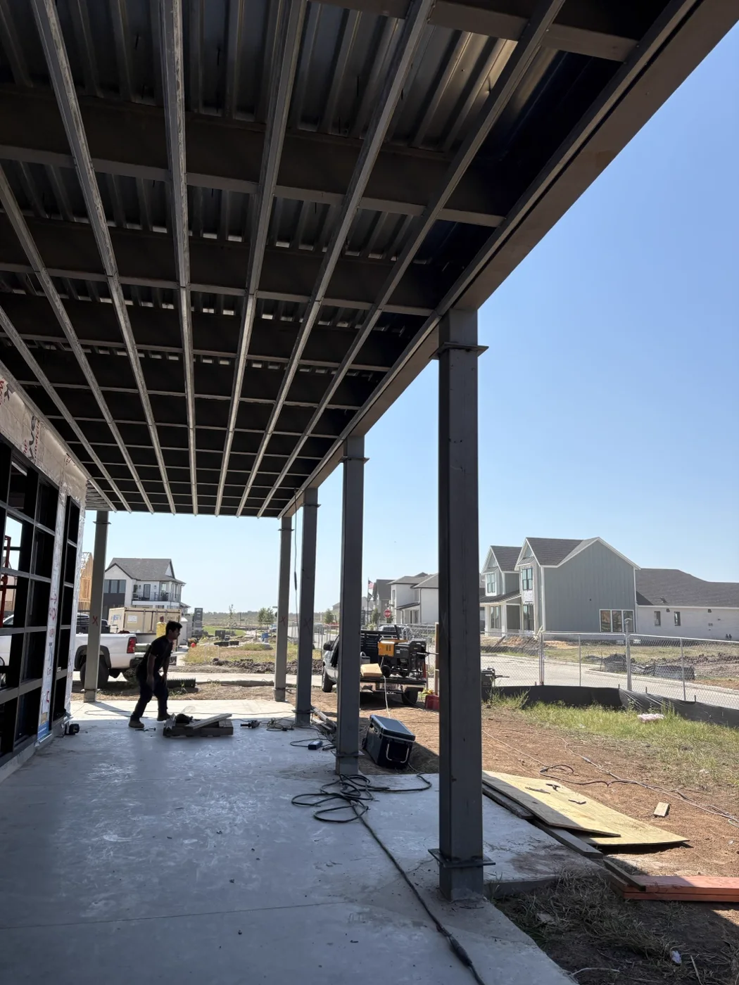 patio-attached-frame.webp Steel columns and roof framing attached to a building, forming a covered walkway
