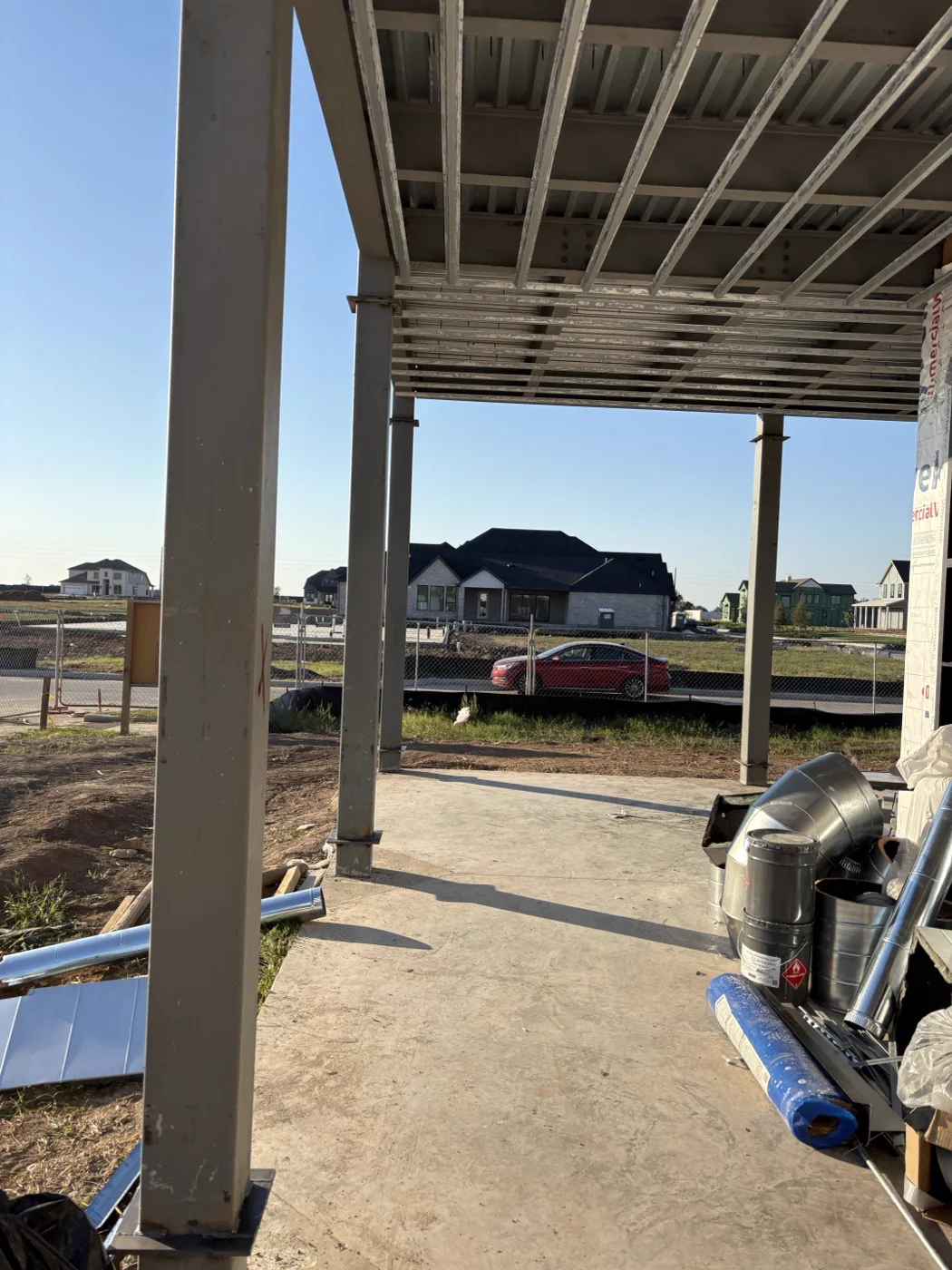 Steel columns and roof framing forming a covered outdoor area over a concrete patio at a residential build