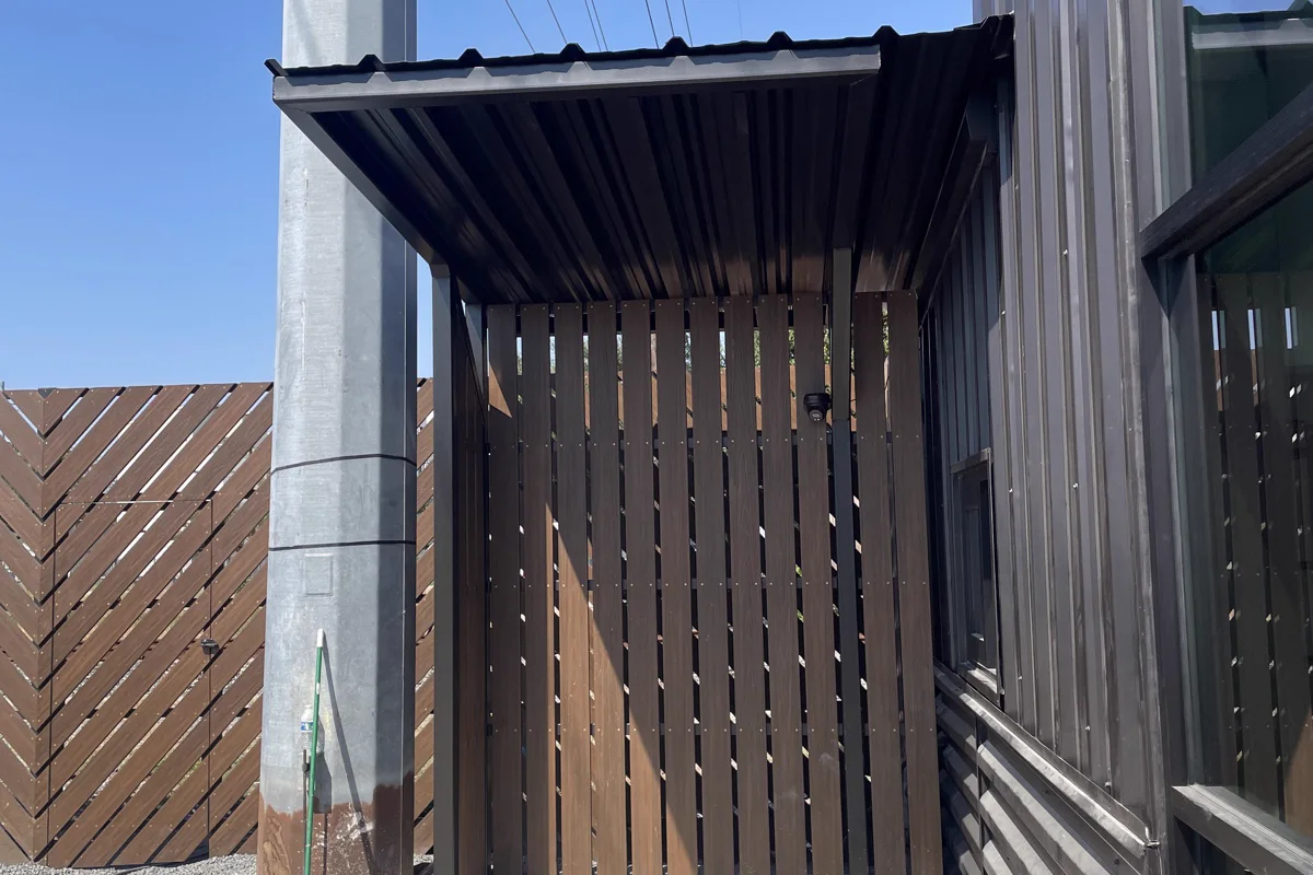 Steel canopy on a column covering a slatted screen enclosure beside a building